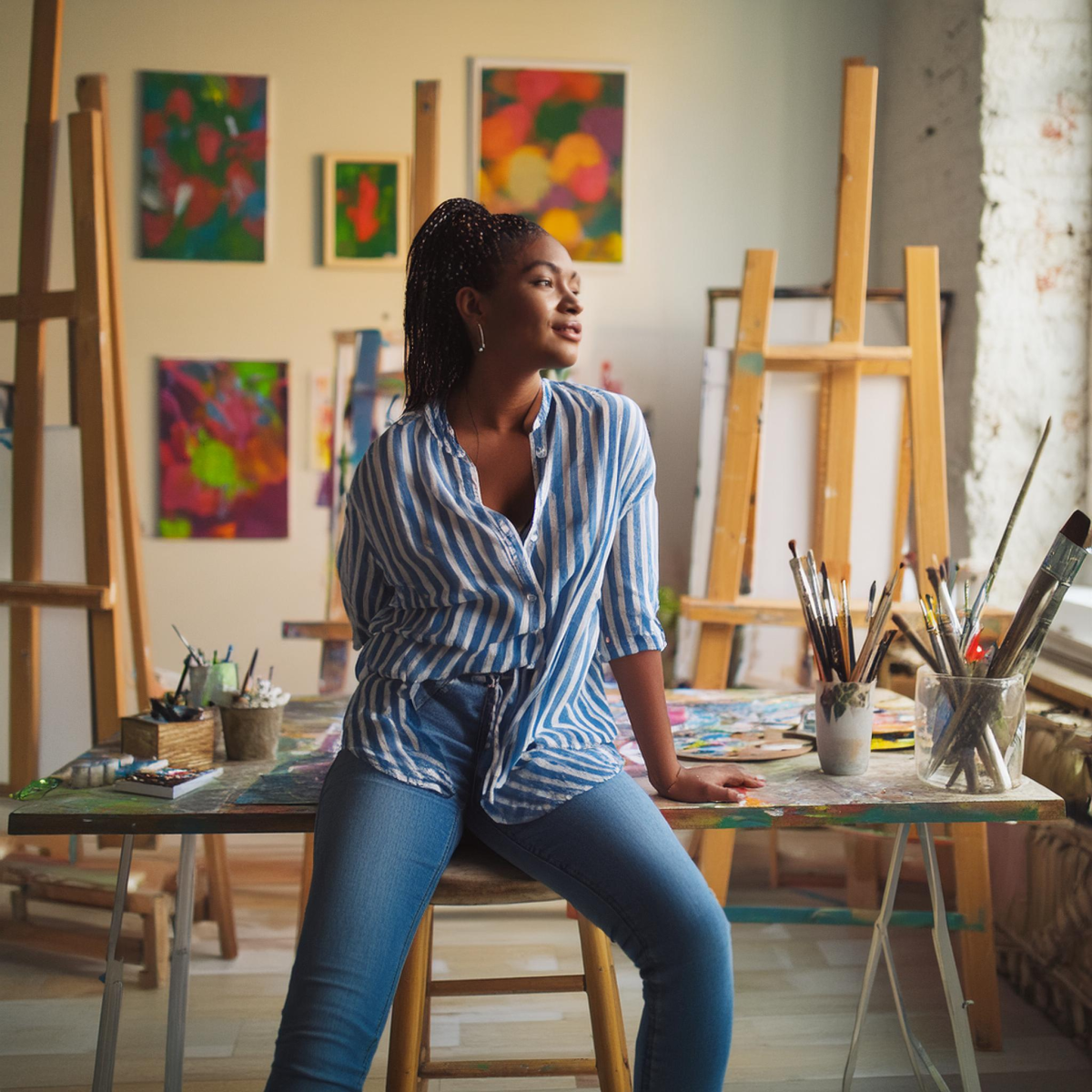 “An artist in his studio sitting at desk looking pensive with tons of paintings and ethereal.” From Image 2. Image Credits: Adobe


